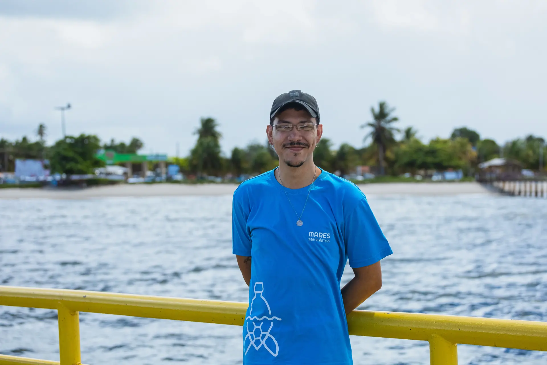 Integrante do projeto com a camiseta do Mares, na balsa, com o rio ao fundo