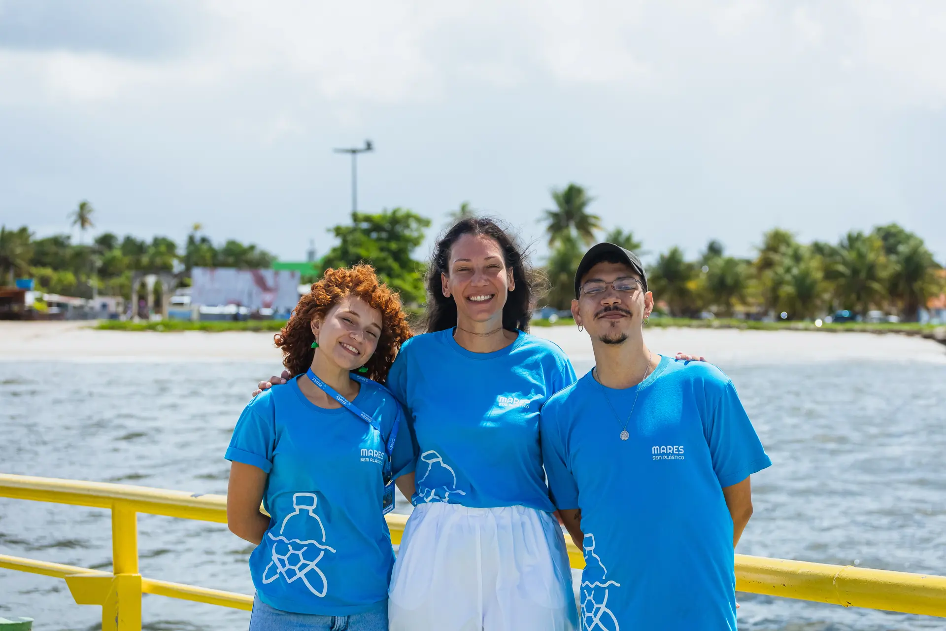 Três integrantes do projeto sorriem na balsa, com o rio ao fundo