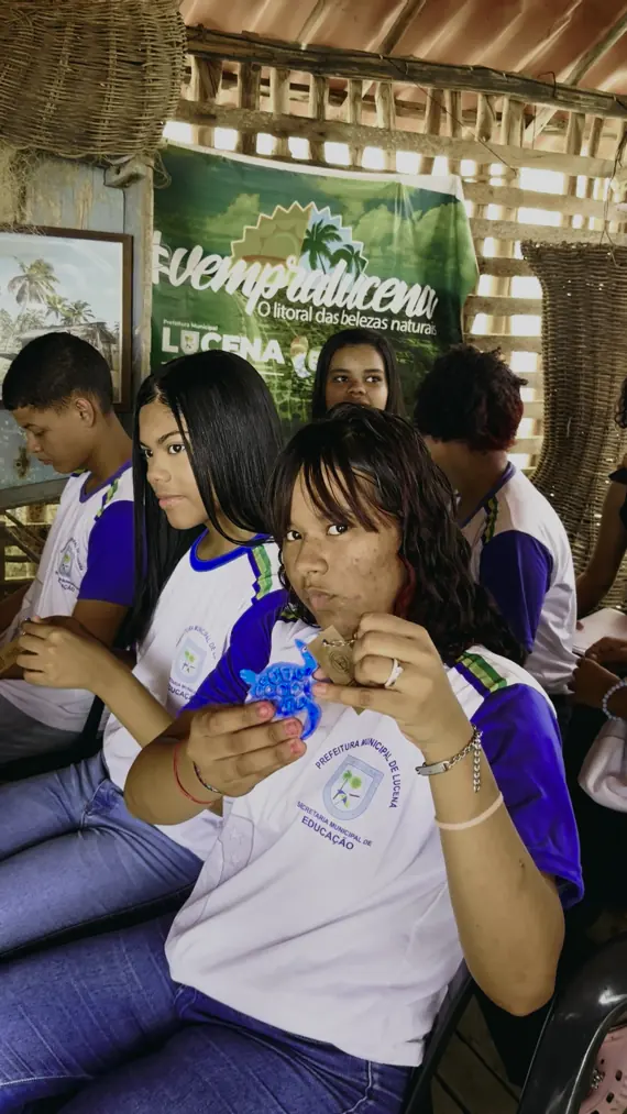 Estudantes de uniforme manuseiam chaveiros de plástico reciclado em oficina
