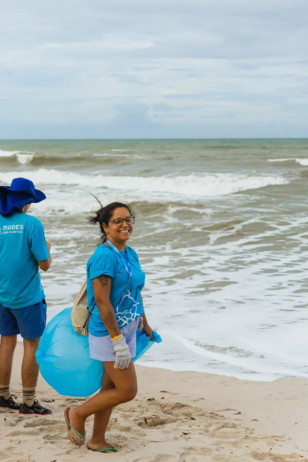 Voluntária com saco de coleta na areia, à beira do mar